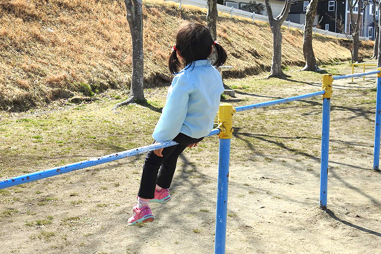 鉄棒に一人で腰掛ける少女