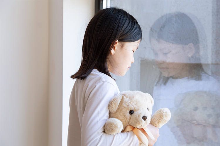 窓際でぬいぐるみを抱き、うつむく少女